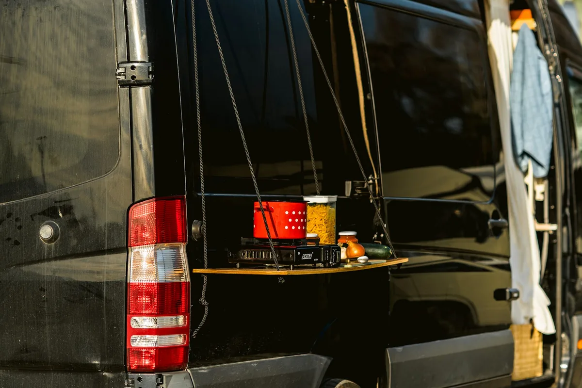 Una furgoneta camper negra con una repisa de cocina plegable en la parte trasera
