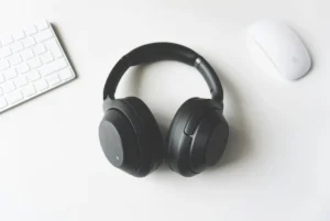 Black over-ear headphones lying on a white desk next to a white keyboard and mouse