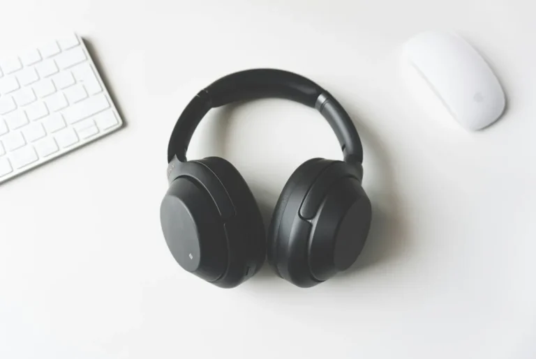Black over-ear headphones lying on a white desk next to a white keyboard and mouse