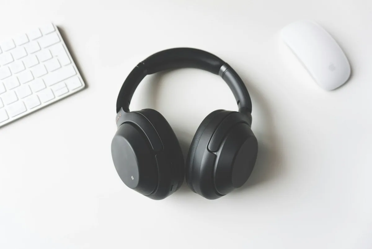 Black over-ear headphones lying on a white desk next to a white keyboard and mouse
