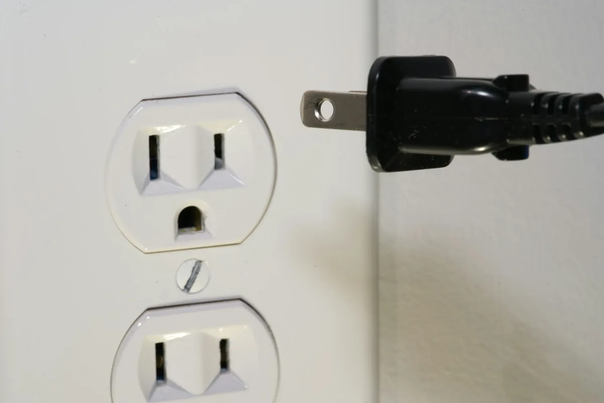 A black two-pin plug held in front of a US wall socket