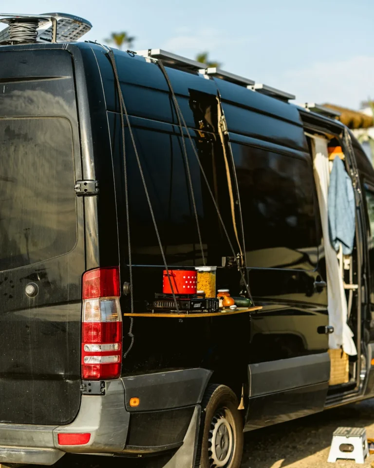 Black van with solar panels on the roof and a small outdoor kitchen shelf on its side