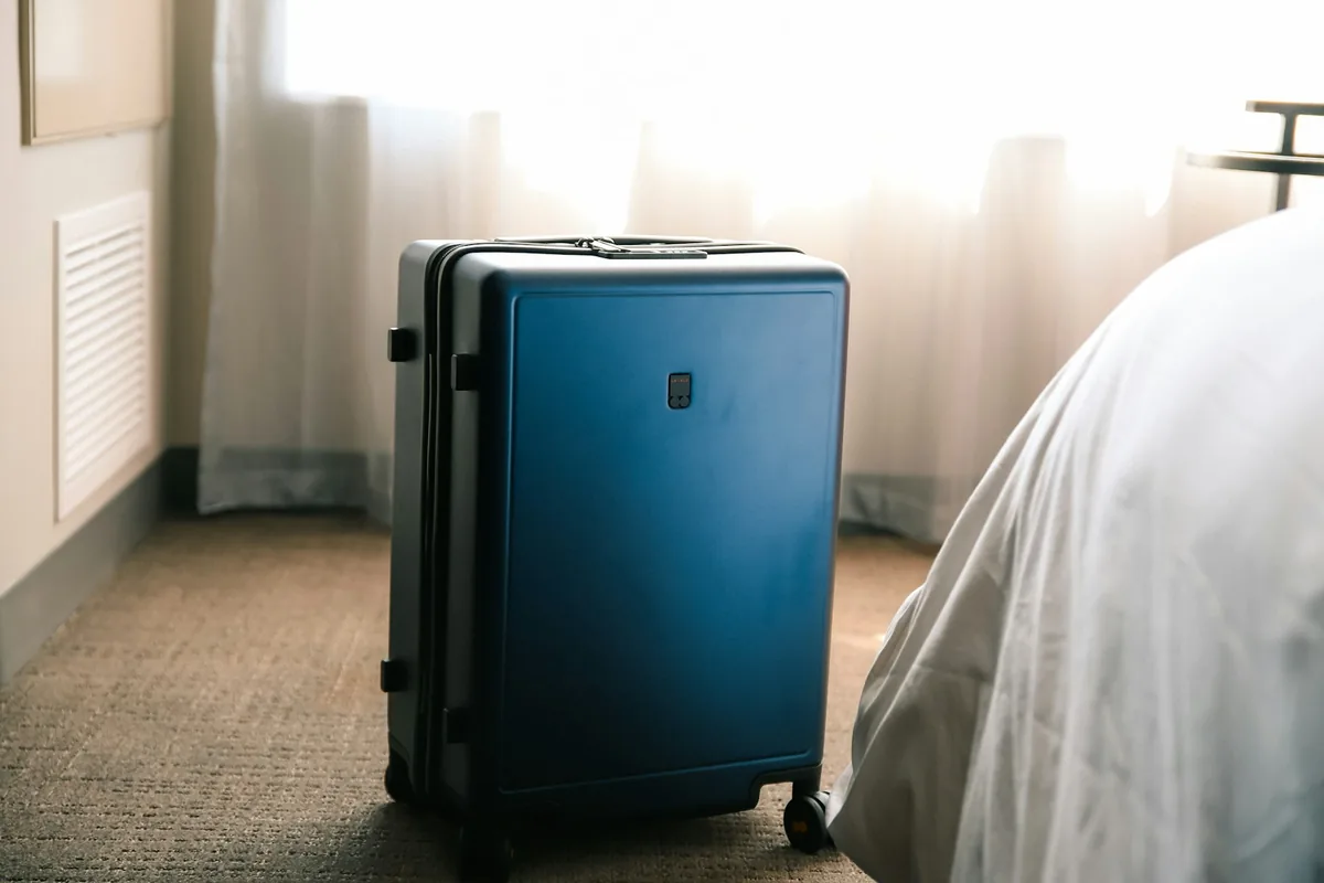 Een blauwe koffer op de vloer naast een bed in een hotelkamer