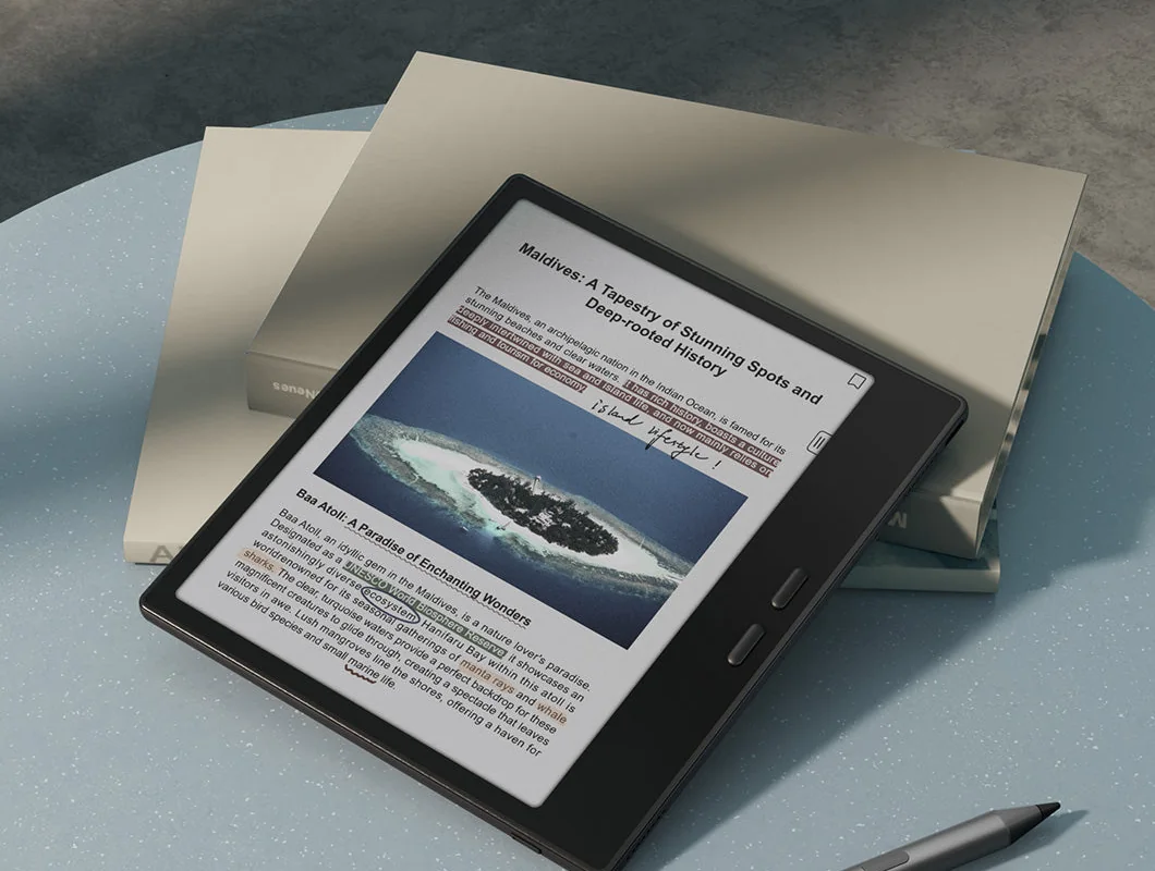 BOOX Go Color 7 e-ink tablet lying on a table with a stylus and a paper book beside it