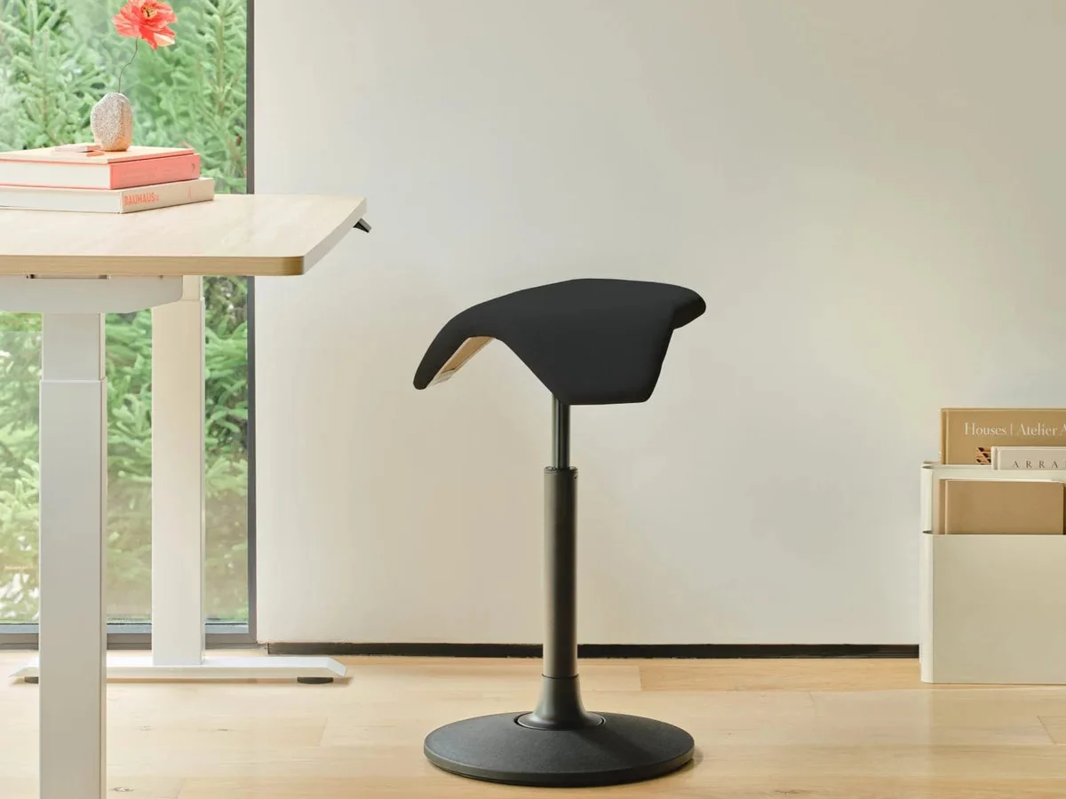 Black Branch Saddle Stool with a wobble base next to a light wood standing desk