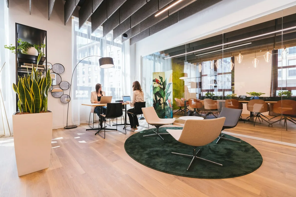 Bright coworking lounge with plants, armchairs and a few people working