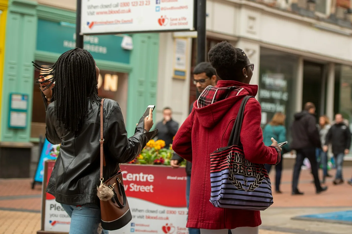Pedestrians with phones on a busy city street, the crowd a Find My or SmartThings network relies on