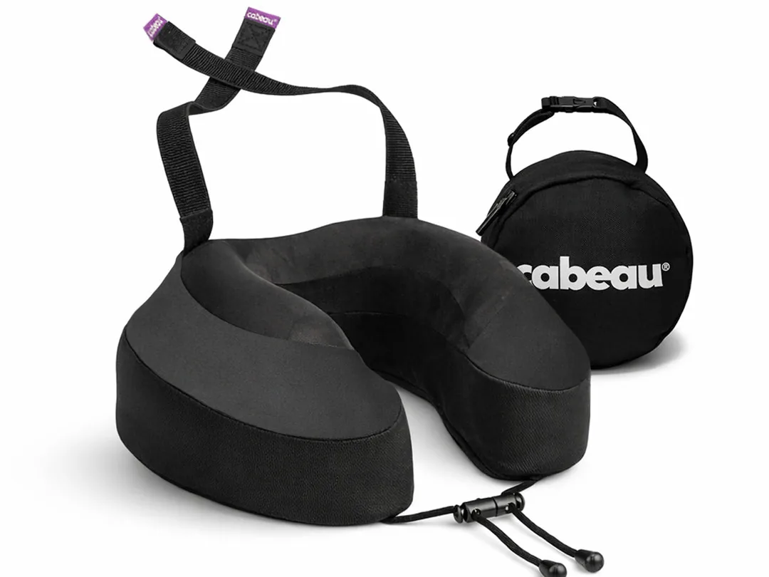 Black Cabeau Evolution S3 neck pillow with its seat straps looped up and the round black carry case behind it