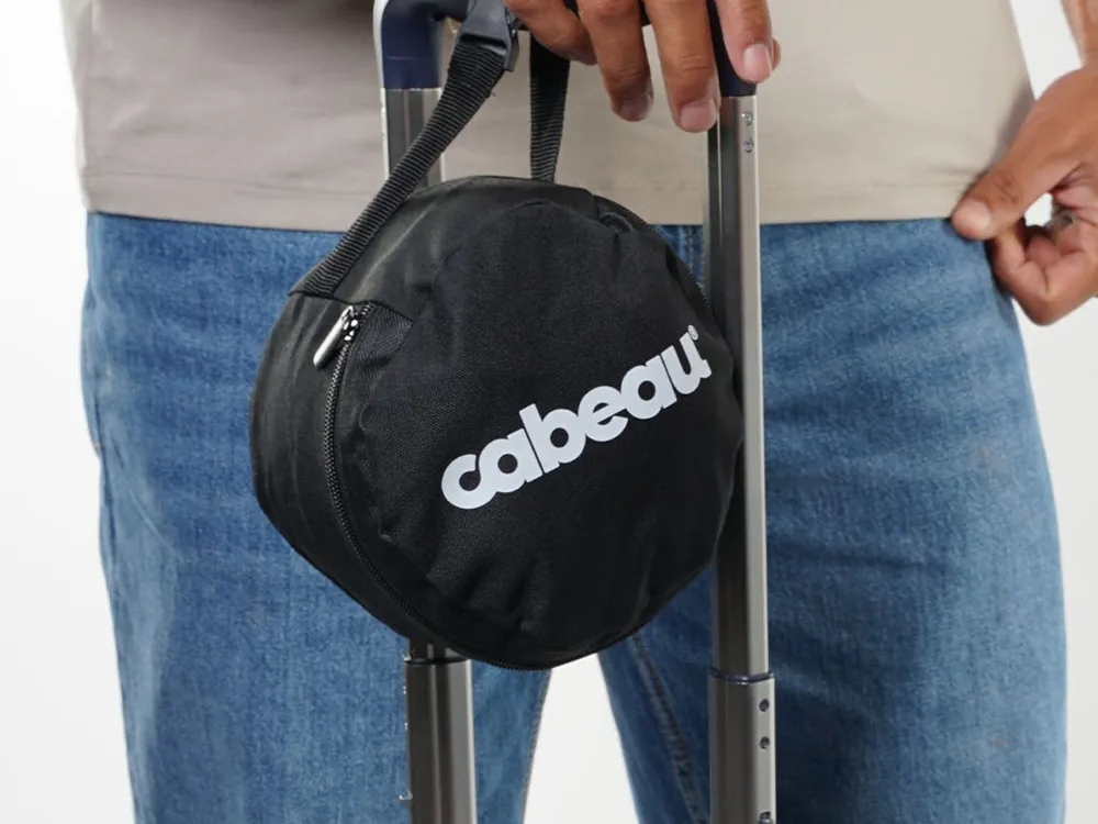 Round black Cabeau travel case with its logo clipped to the handle of a suitcase