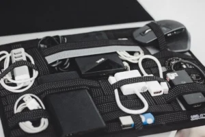 Cables, chargers and small electronics arranged on a black board with elastic straps