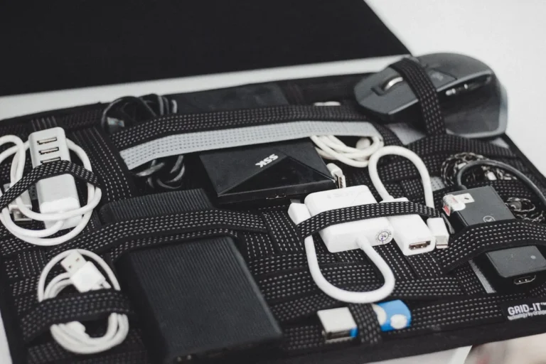 Cables, chargers and small electronics arranged on a black board with elastic straps