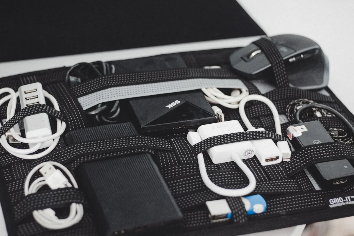 Cables, chargers and small electronics arranged on a black board with elastic straps