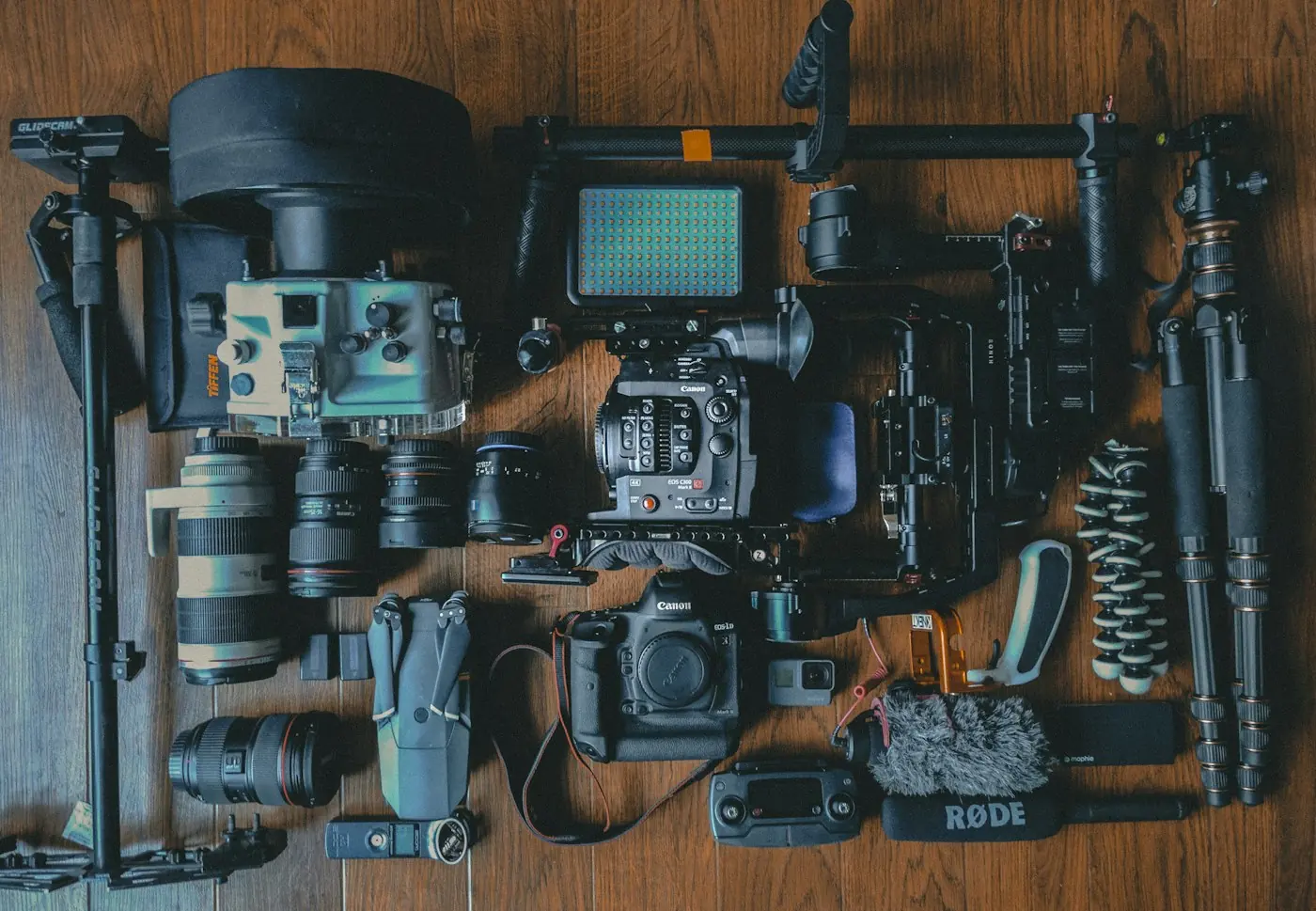 Flat lay of camera bodies, lenses, a tripod, a light and a gimbal on a wooden floor