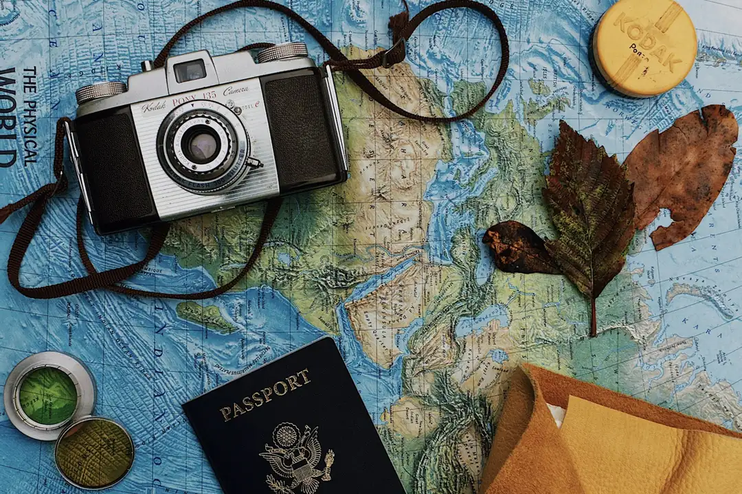 Old film camera, a passport and dried leaves on a map