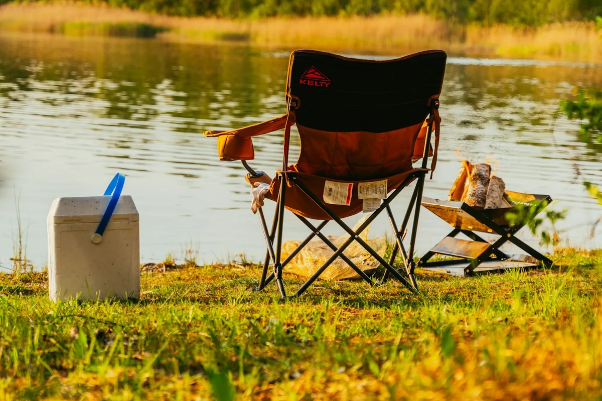 Camp chair and a white ice cooler on a grassy lake shore at golden hour, the old way to keep drinks cold