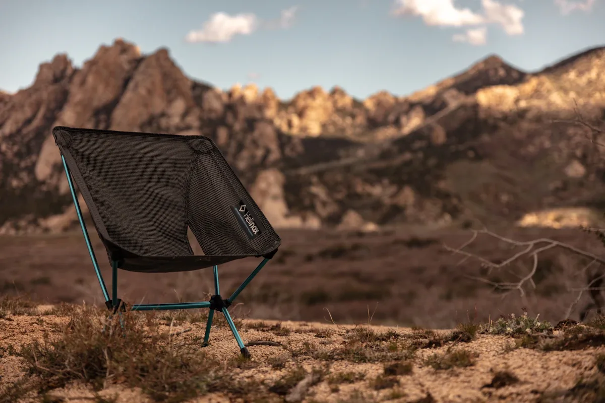 Een enkele zwarte opvouwbare campingstoel met blauwe poten op een rotsachtige heuvel met bergen op de achtergrond