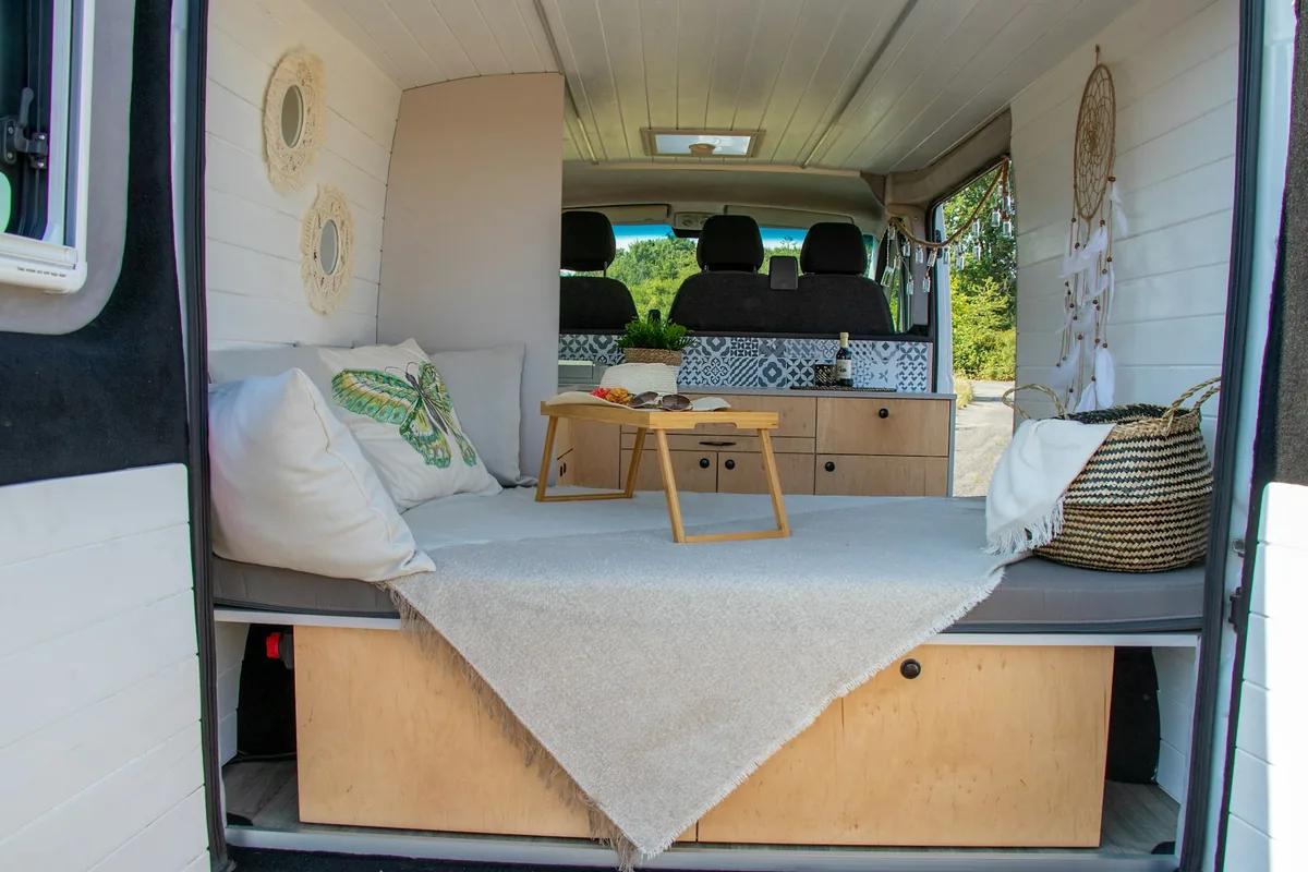 The inside of a camper van with a bed, a small table and a roof vent