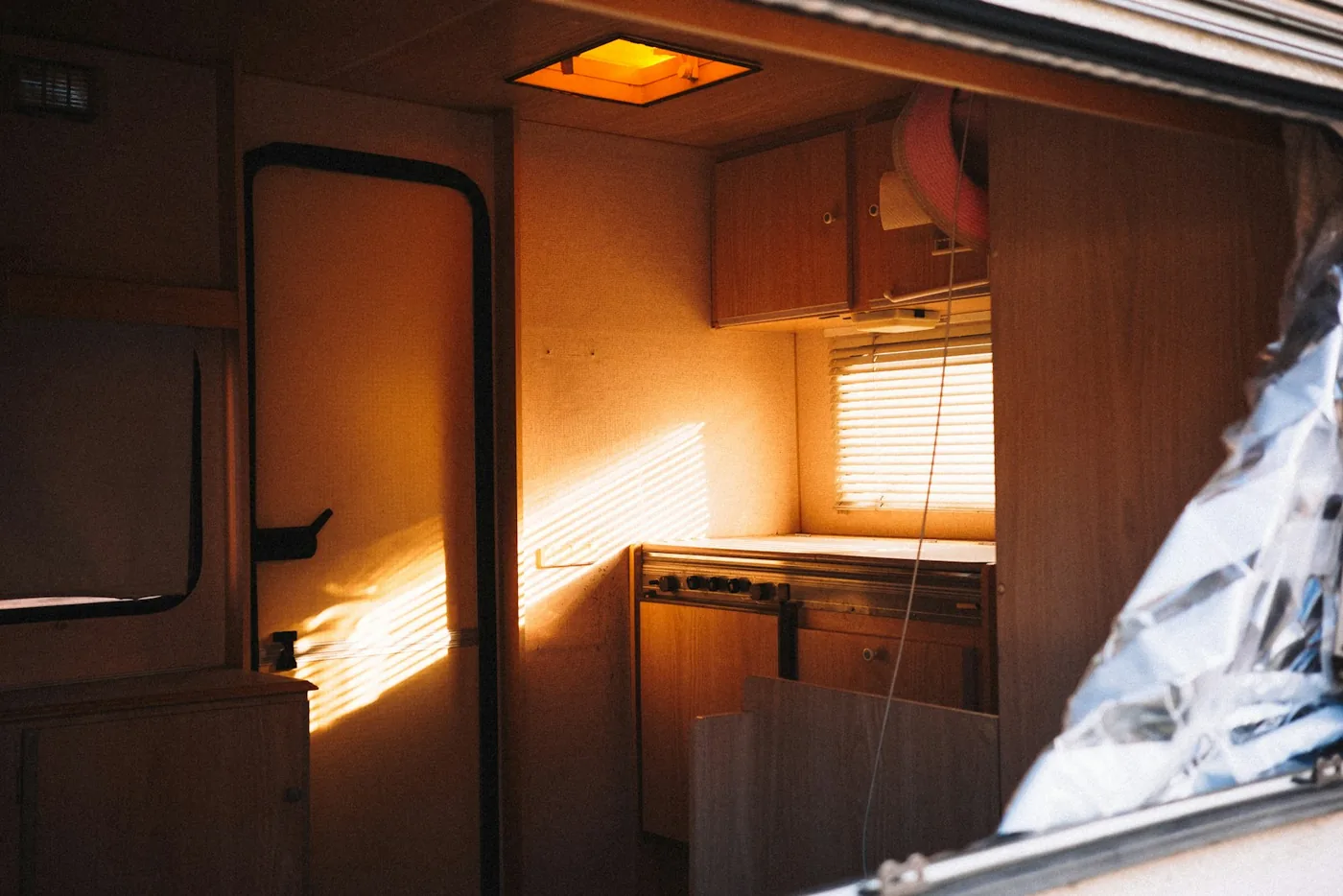 Inside a small camper with wooden cabinets and warm evening sunlight coming through the door