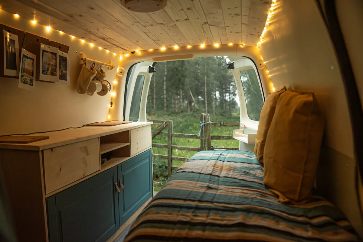 Inside a self-built camper van with a wooden ceiling, handmade cabinets and warm string lights