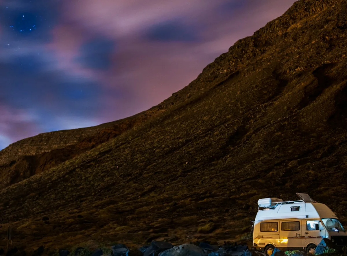 Camper van parked at the foot of a mountain at dusk