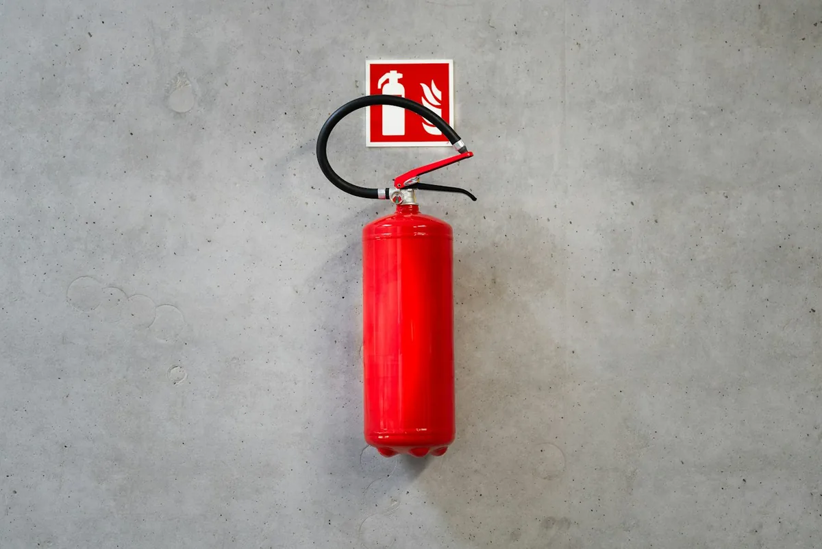 Red fire extinguisher mounted on a grey concrete wall with a small fire safety sign above it