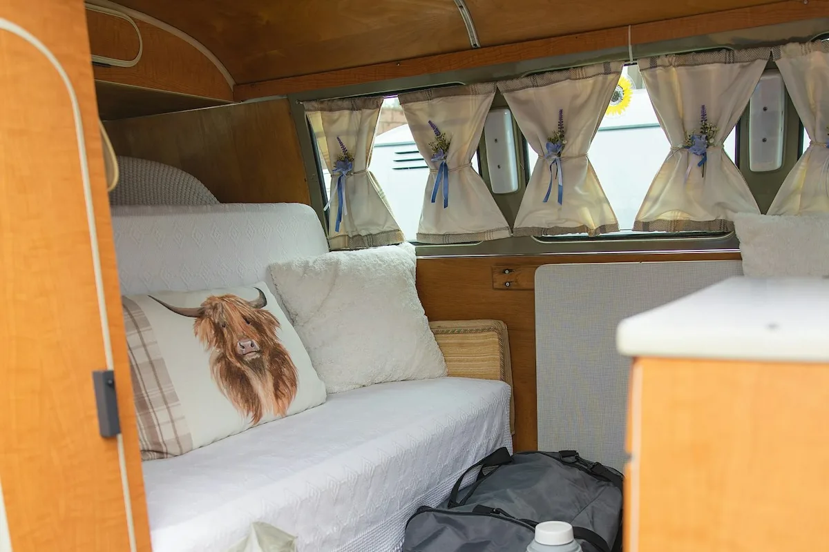 Cozy camper van interior with a sofa bed, curtains, boots and a bag on the floor