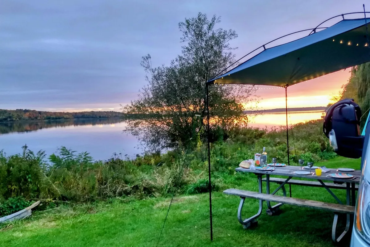 Een picknicktafel onder een luifel naast een camperbus bij een meer tijdens zonsondergang