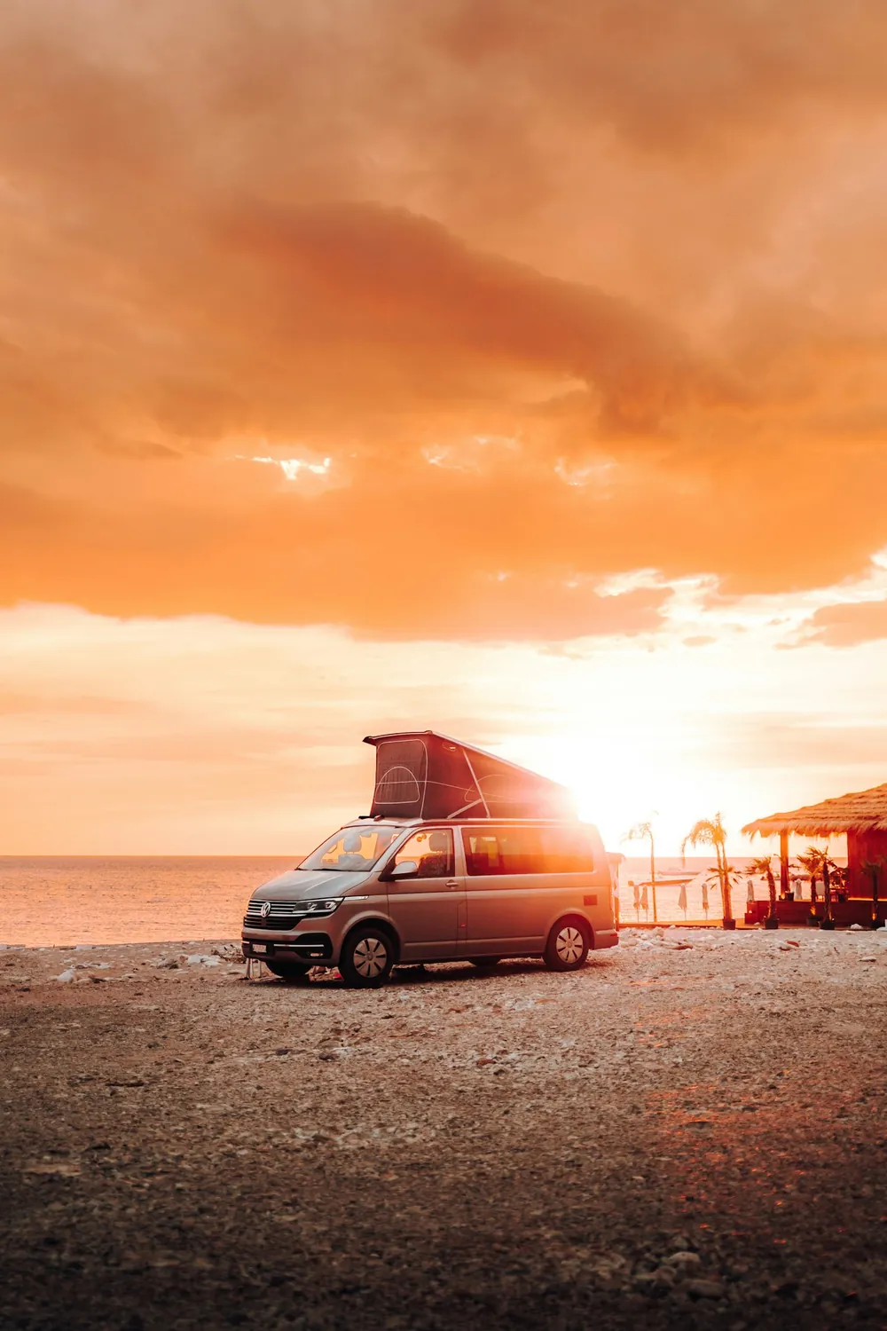 A camper van with a pop-up roof parked on a beach at sunset