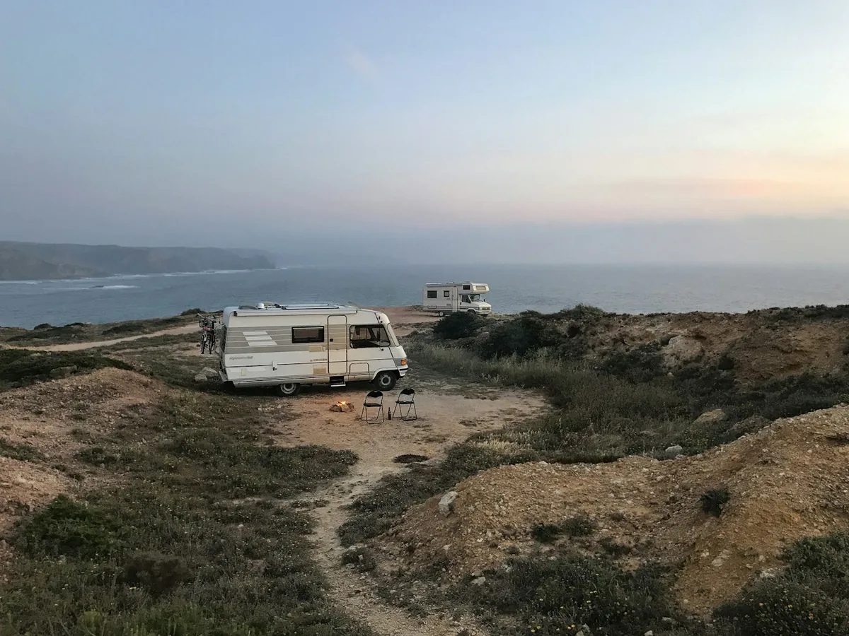 White motorhome parked on a grassy clifftop at dusk above the sea, with a second motorhome in the distance