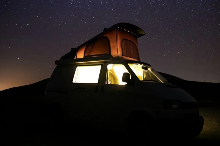 A camper van with a pop-up roof and lit windows under a starry night sky