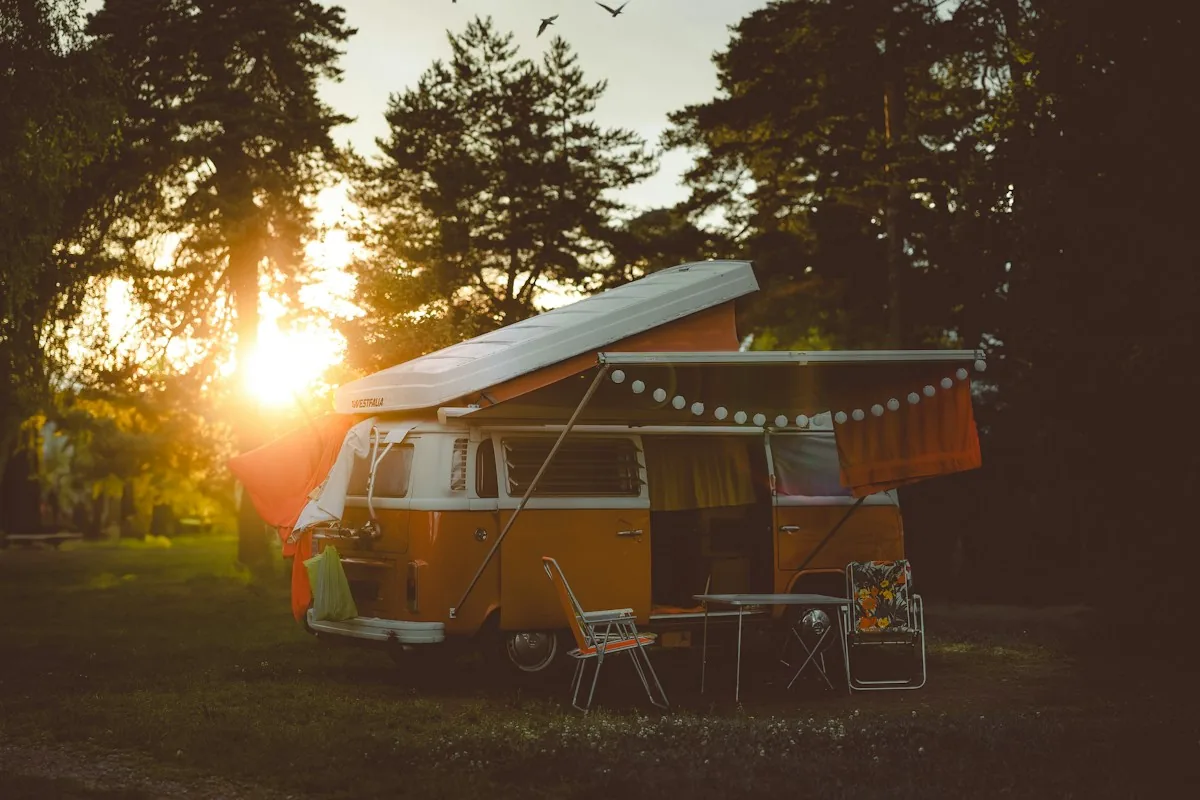 Orange camper van parked at a forest campsite at sunset
