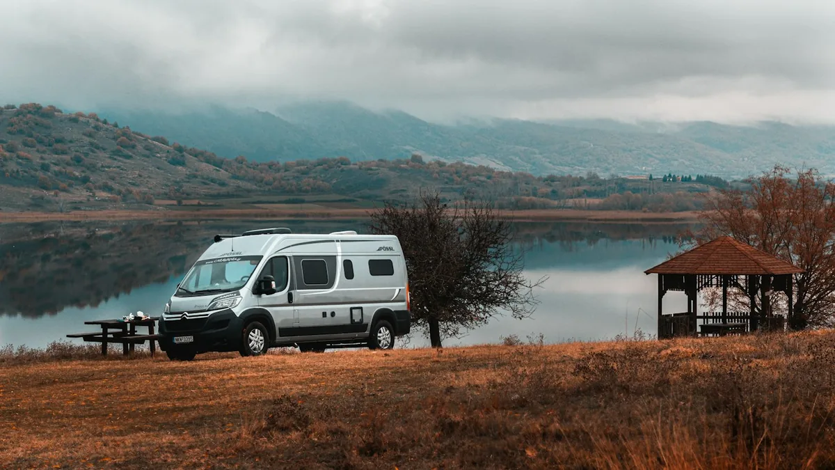 Silver campervan parked on a grassy lake shore with misty hills behind it