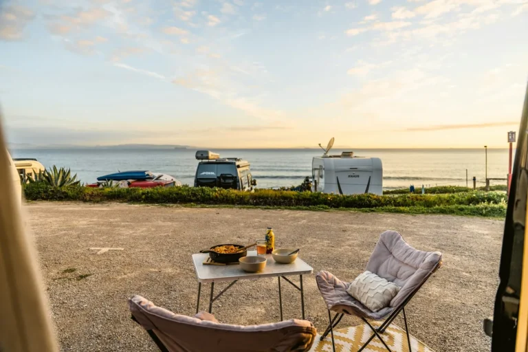 Campervans parked by the sea with a small table and chairs set up outside