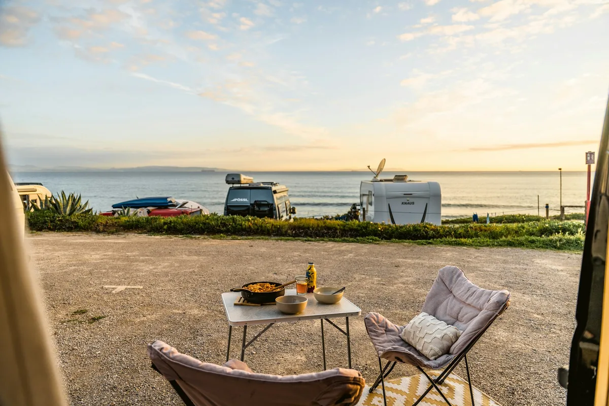 Campervans parked by the sea with a small table and chairs set up outside