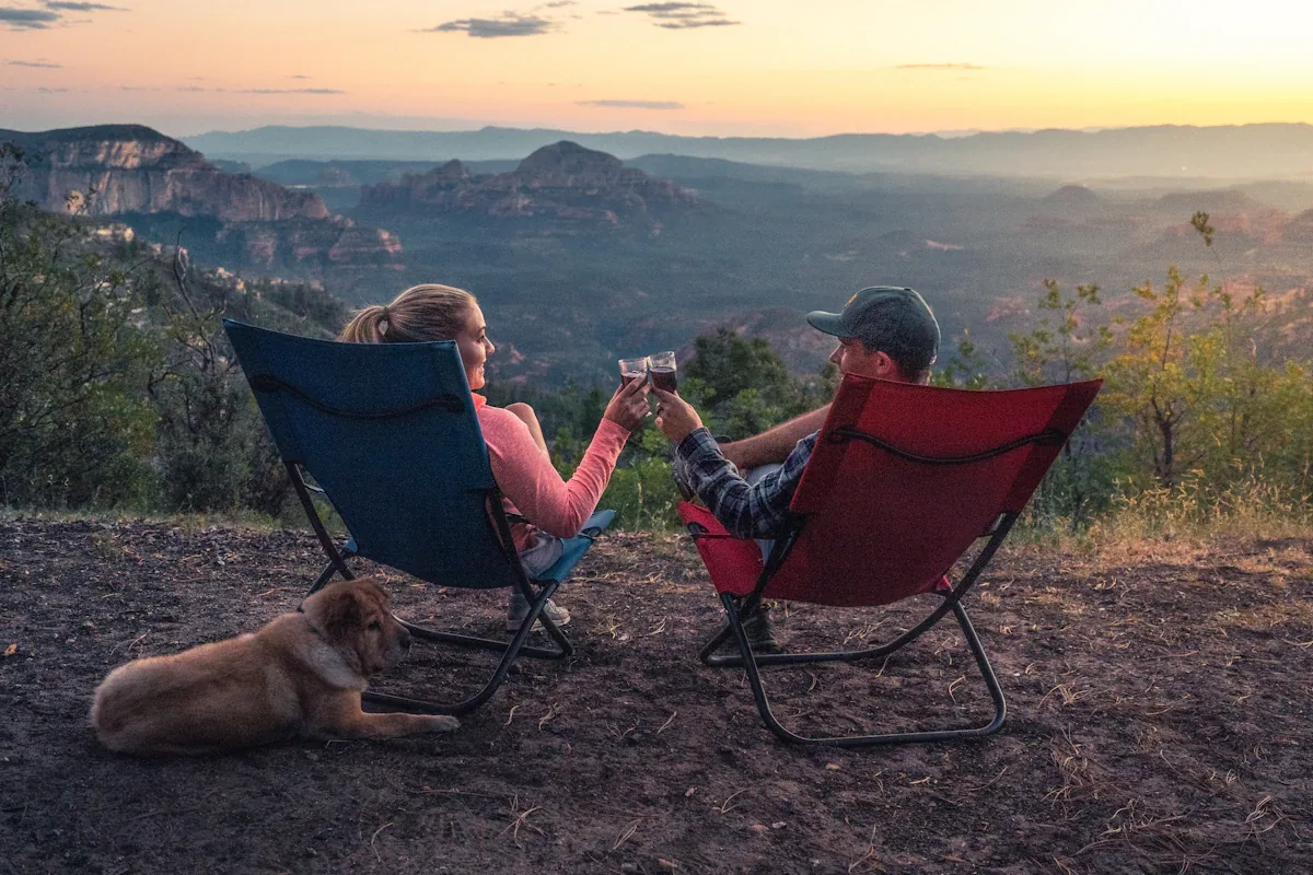 Two people in camp chairs with a dog at a mountain viewpoint at dusk