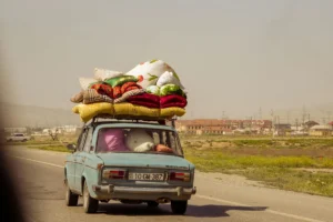 An old car with luggage piled on the roof driving on a road