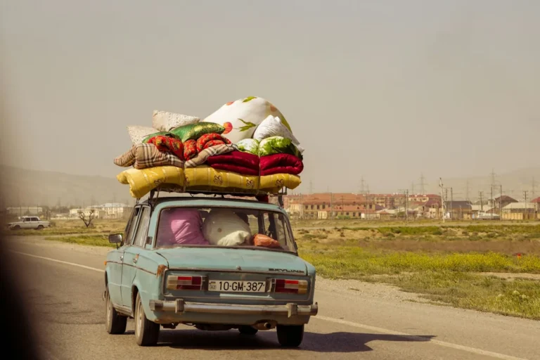 An old car with luggage piled on the roof driving on a road