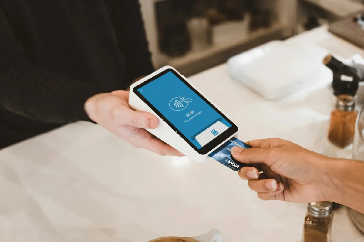 Hand holding a card to a handheld card reader on a cafe counter