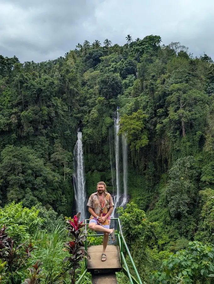 Chenzo, founder of NomadsToolsLab, sitting on a wooden lookout in front of a tall waterfall in the green jungle of Bali