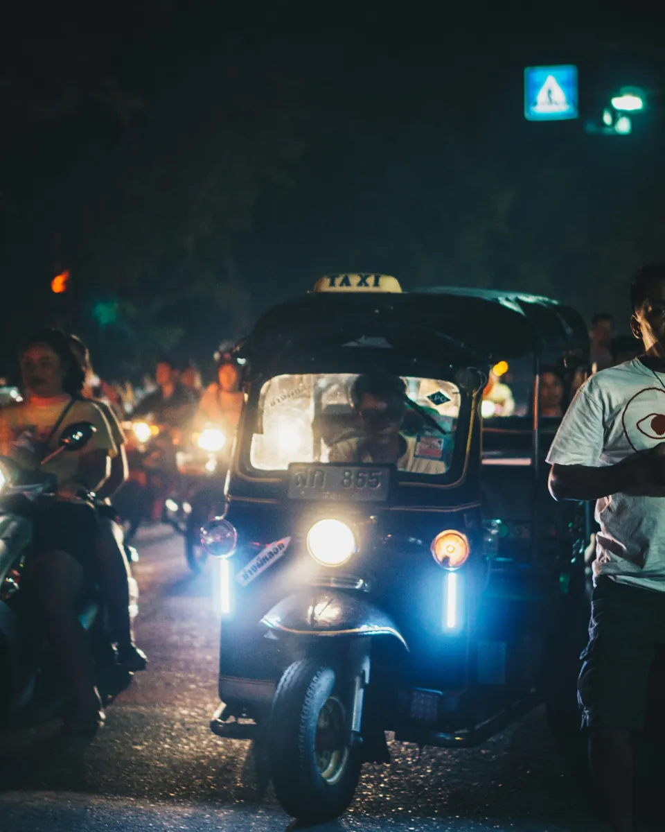 Taxi tuk-tuk with a taxi sign in dense night traffic with motorbikes