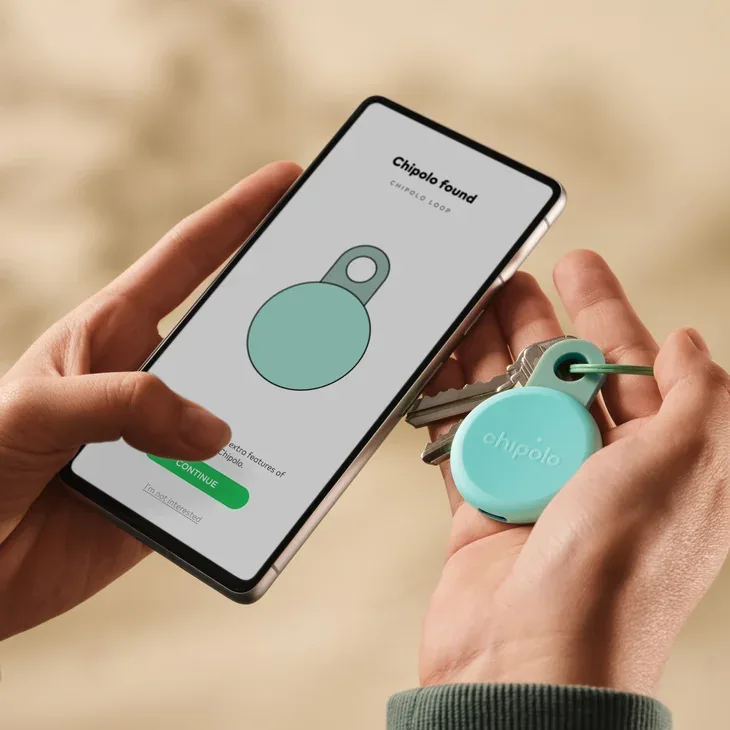 Hands holding a phone with the Chipolo app next to a mint Chipolo LOOP on a key ring