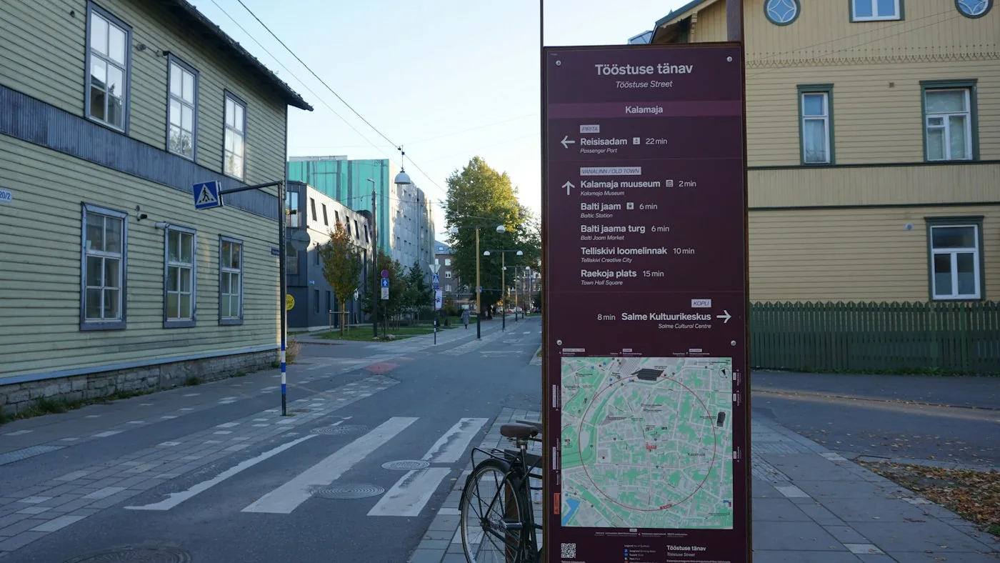 City street with a map sign beside a pedestrian crossing and wooden houses