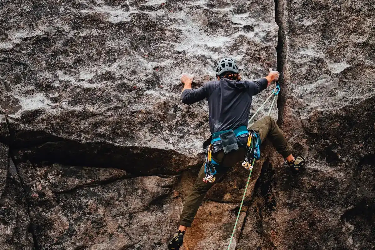 Climber in a helmet and harness on a dark rock face with a rope running down