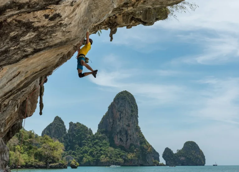 Climber on an overhanging rock cliff above the sea with rocky islands in the distance