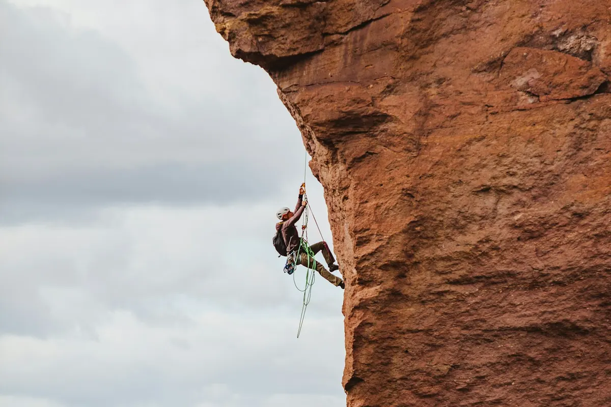 Climber in a helmet hanging on a rope beside a red rock overhang