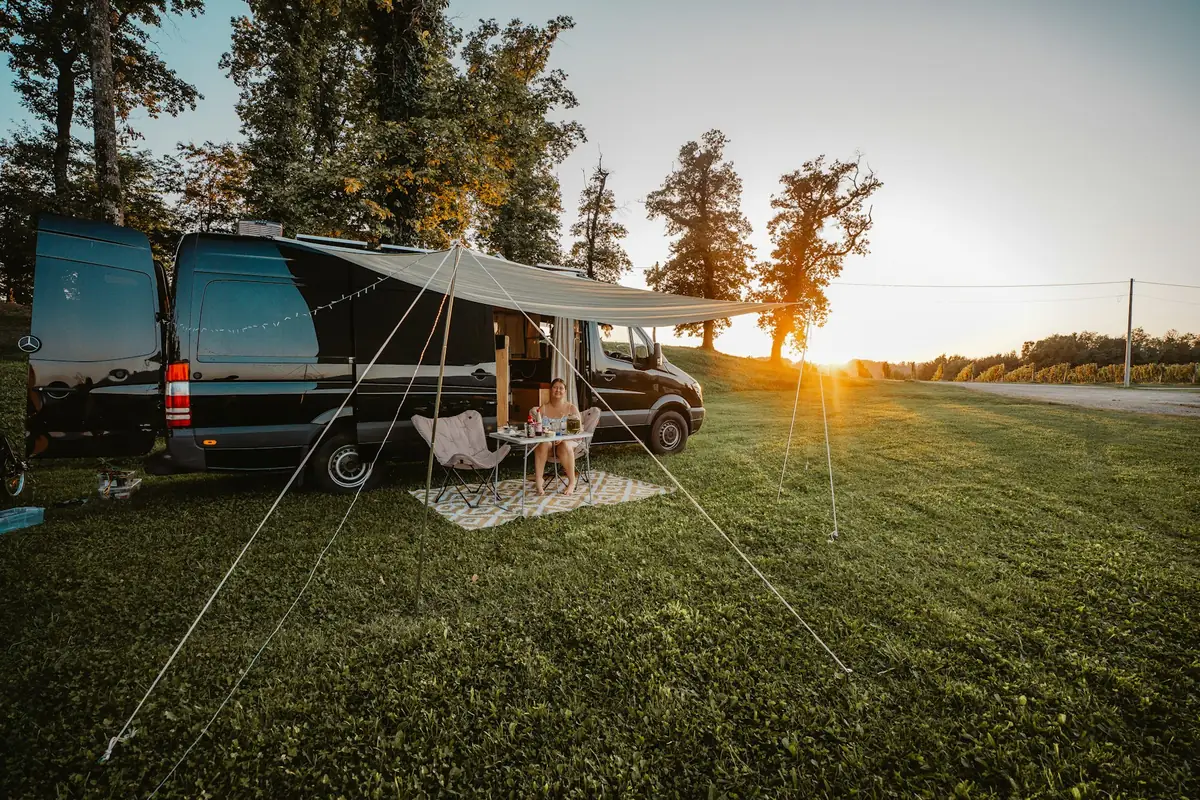 A couple relaxing under a camper van awning at sunset on a grassy campsite