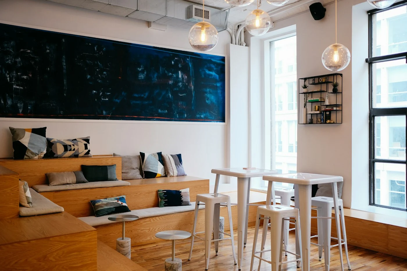 Bright coworking space with white wooden tables, stools and a long bench with cushions