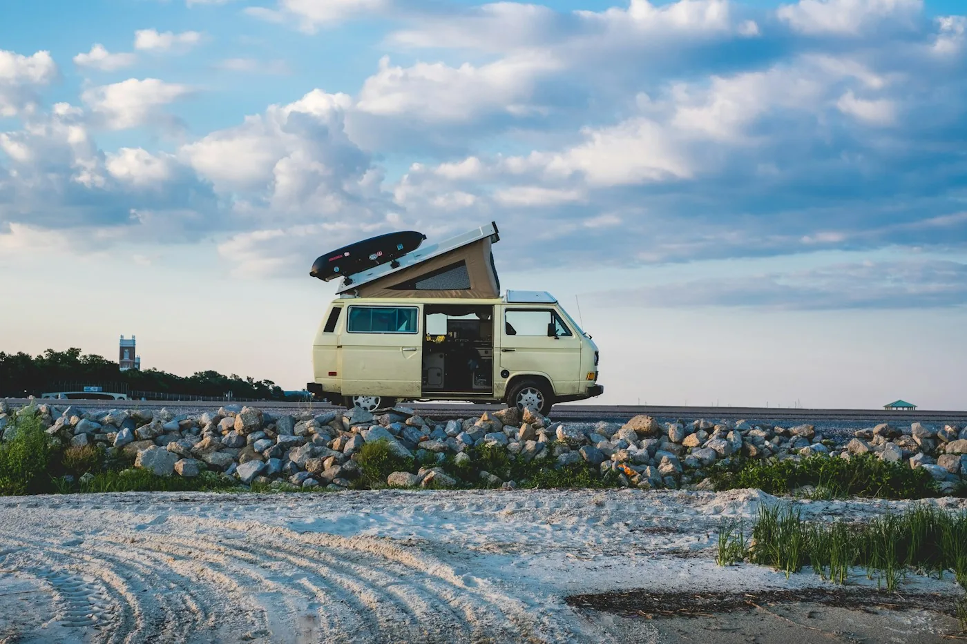 Camper van color crema con techo elevable aparcada en una playa bajo un cielo nublado