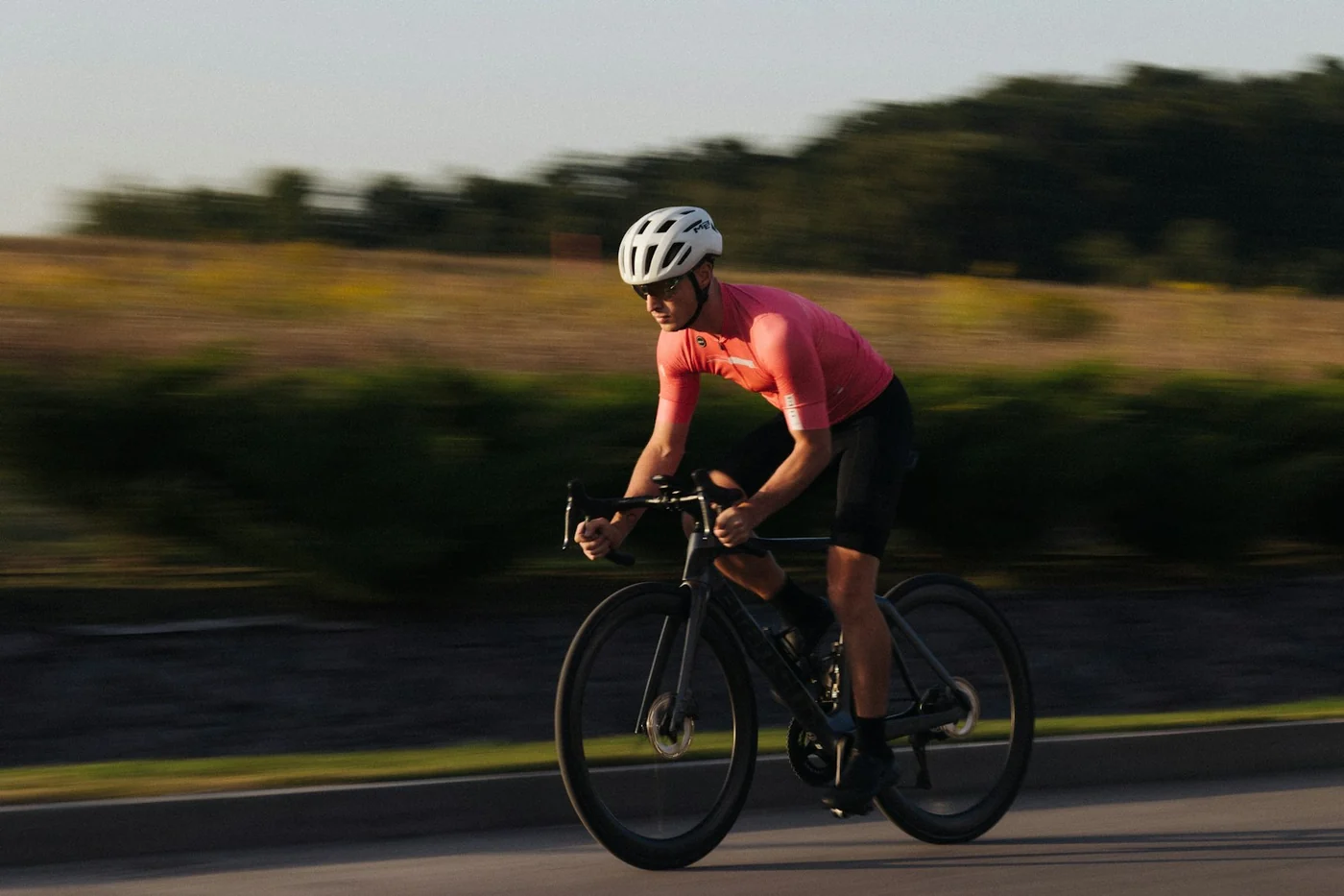 Radfahrer in pinkem Trikot und weißem Helm fährt schnell auf einer Straße mit unscharfem grünem Hintergrund