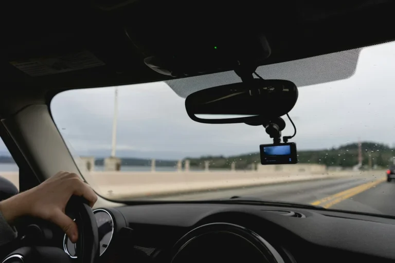 Dash cam mounted behind the rear-view mirror of a car on a highway, driver hand on the wheel